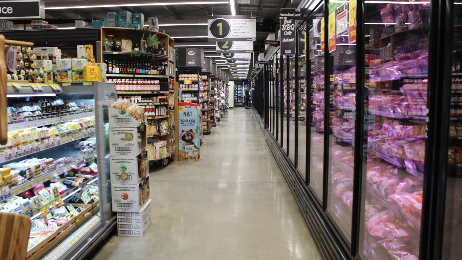 An image showing dairy items on the left shelves. At the ceilings are hanging boards that have a summary of food categories from 1-6 for each rack. Hanging board no. 1 is for breakfast foods, coffee & tea, biscuits, juice, jams & spreads, and health & wellness. Boxes containing food packages can also be seen in the pathway.