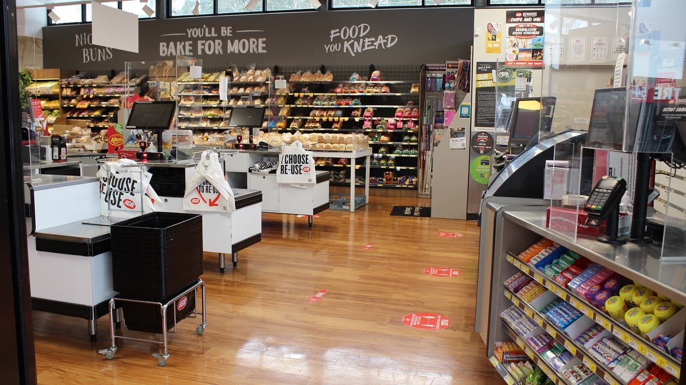This payment section of the grocery store offers three available white counters. There is a selection of bread items on display to the right with signage above stating “Night Buns”, “Bake for More” and “Food You Knead”. The plastic shopping bags are also available in each counter that has a reminder to the customer: “I choose. Re-use”. Two more counters are available at the other side of this section with a range of gum and lollies on display.