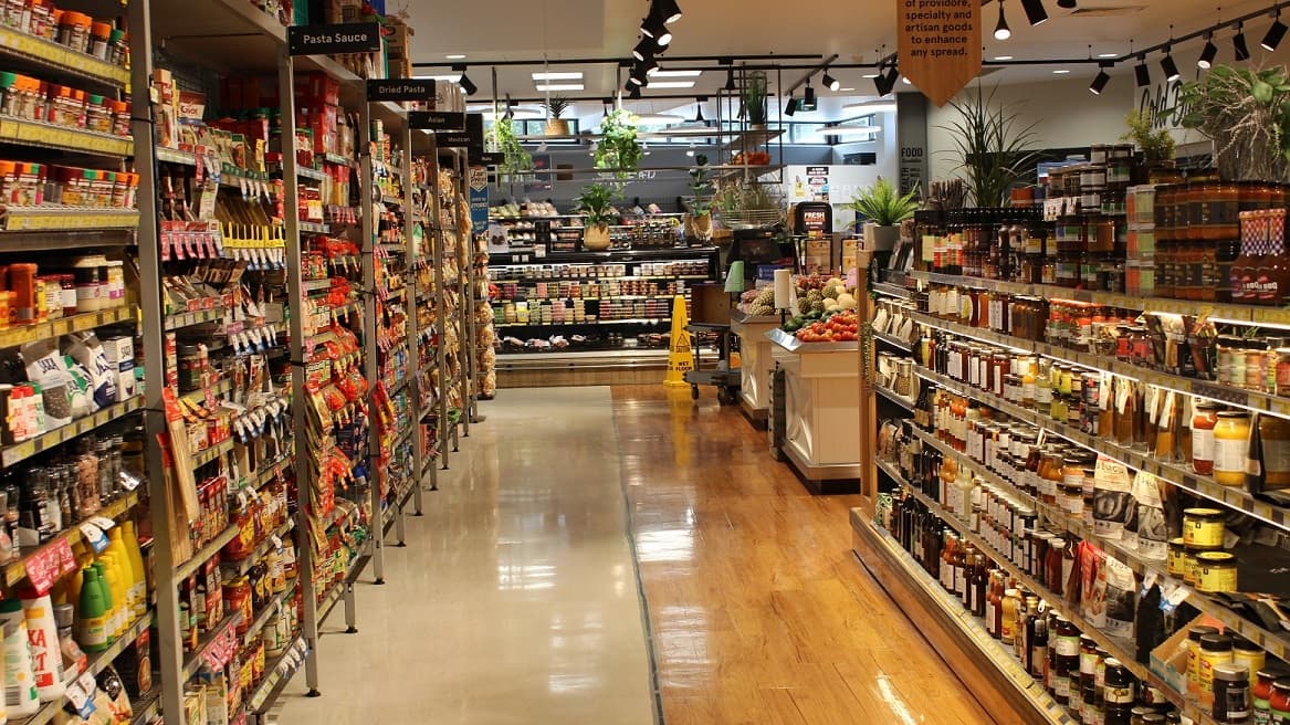 This is a closer view of the divided sections of the fruit and vegetable section and the pasta aisle. Half of the aisle floor is brown that designates the fruit and vegetable section while white on the other side indicates a different section of the store which is the pasta aisle. At the right side, which is the pasta aisle, with different brands of pasta sauce, dried pasta and other ingredients used in cooking pasta.
