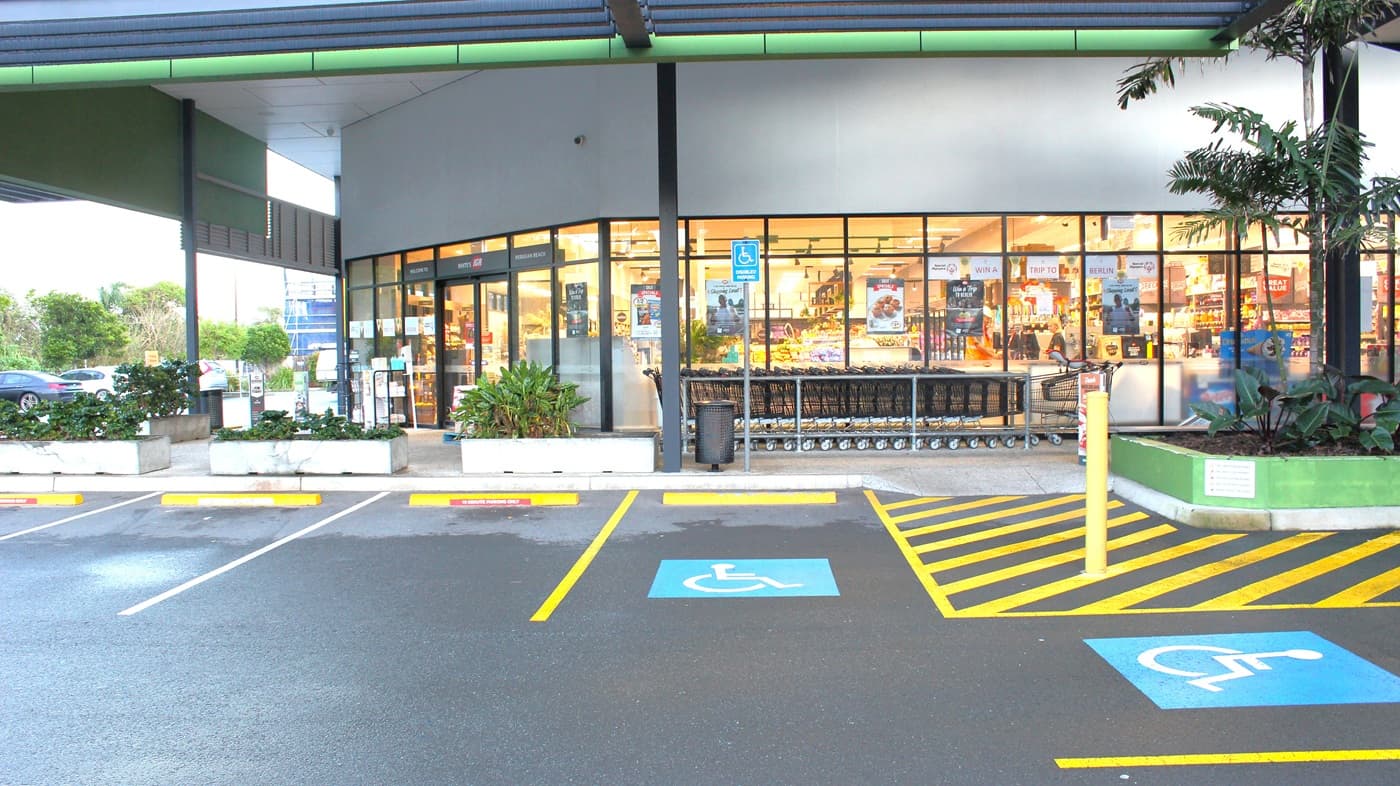 Accessible parking spaces right outside the entrance of the IGA shopping store. The parking area has yellow stripes and white lines. Accessible parking signs in blue and white are drawn in the parking area for persons with mobility issues. Black shopping carts are carefully arranged outside the store.