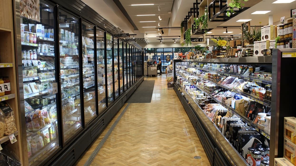 Opposite view of the previous image. The content of the fridge is now visible and the fresh organic and vegetable labels can be seen clearly. Opposite the fridge are other food consumables and condiments.
