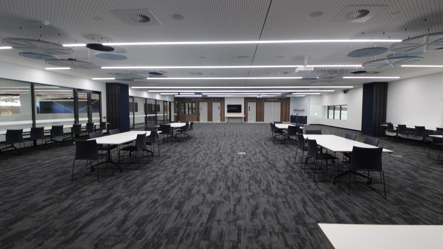 This is the view of function room 1 from its main door. Immediately on the left side of the door is the signage that says “Function Room 01” with a people sign icon on it. The door’s casing is black with silver door handles. The function room is large enough that guests have a wide space good enough to walk around. The room view looks pleasant as the bright fluorescent lighting and white and blue round ceiling ornaments is a contrast to the grey carpeted floor.