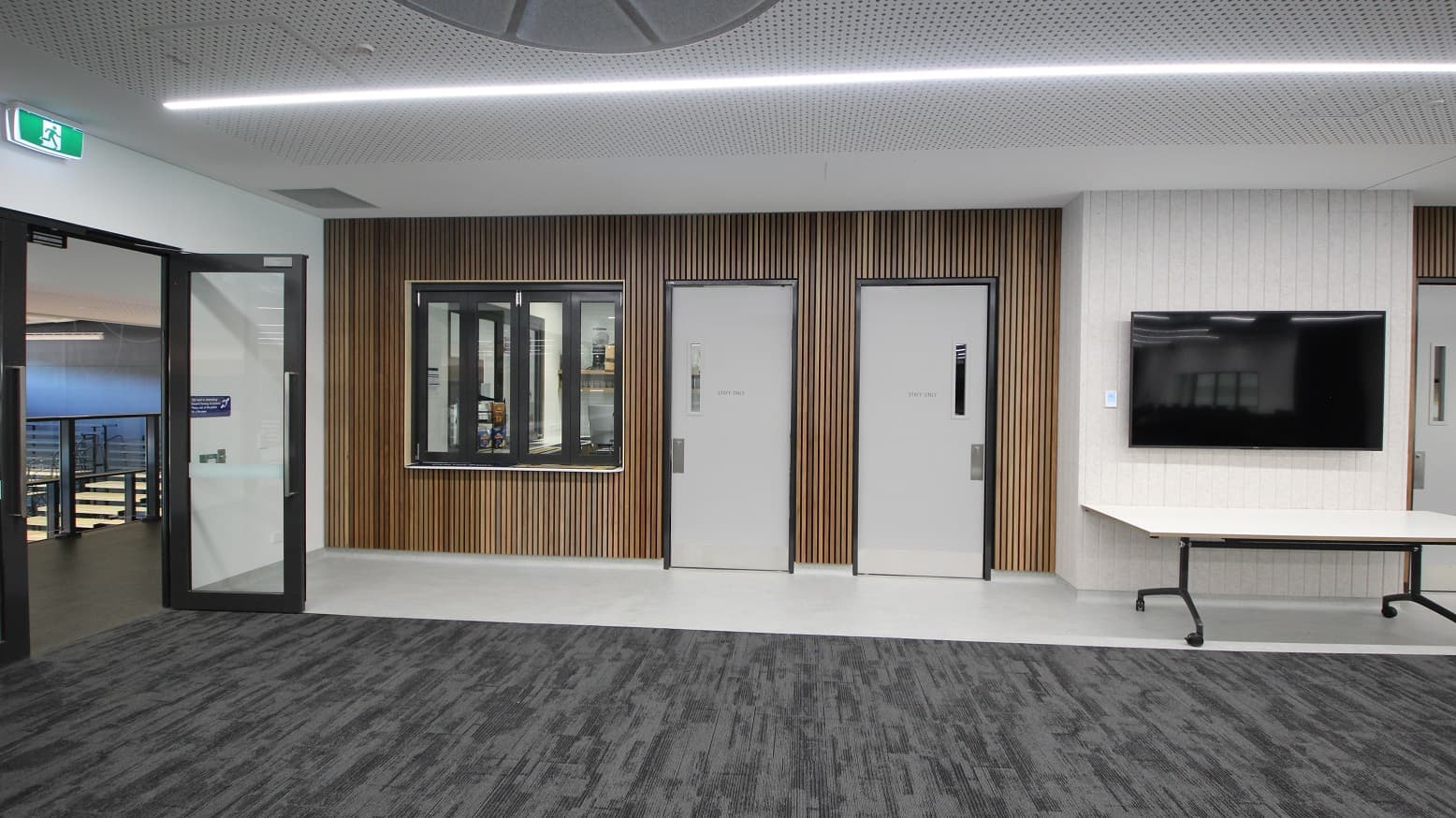 This is the end side of the function room where the staff room is. It has two doors that both have a signage that says “Staff Only”. These doors are painted white with black casing. On the left side of the door are the glass windows where you could see what’s inside the staff room. On the right side of the second door is the white wall where a huge television is mounted, below it is a long white table. The room’s left side is where another manual door is placed that is accessible by the guests.