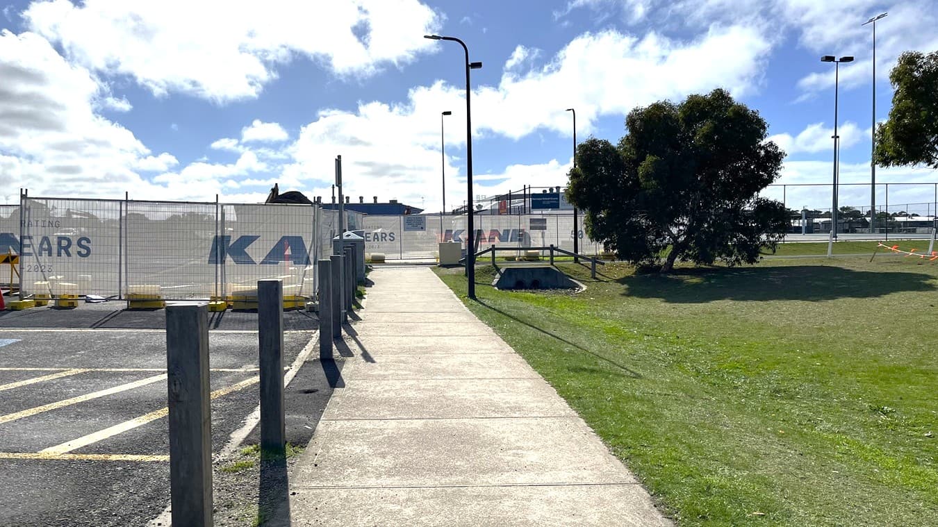 View of the path to access Wurdi Baierr stadium. Path begins alongside construction on the left and a grassy area on the right.