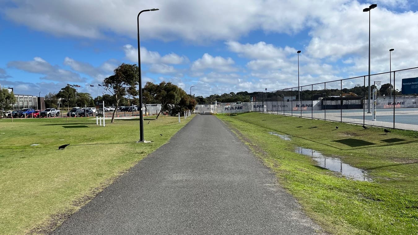 View of the path from Wurdi Baierr stadium towards the disabled car parking. Here, the netball courts are on the right and the oval is on the left. You might hear netballer's playing on this section of path.