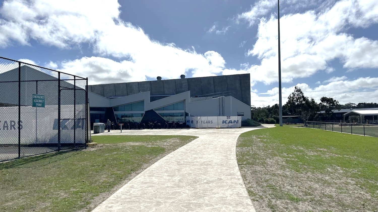 The view of the path towards Wurdi Baierr stadium, closer to the entrance. The fence of the netball courts are on the left and the soccer fields and path towards the school are on the right.