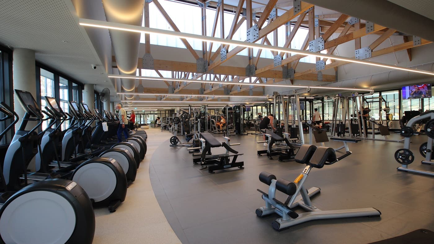 To the right of the staircase is the Gymnasium at Yawa Aquatic Centre. It can be distinguished by a black circular signboard on the left glass door which contains the word “Gym”. This facility also has an ash-hardwood floor and a white ceiling with aesthetic holes. Seen through the glass doors are different pieces of equipment for exercise and a number of potted plants just beside the entry pathway.