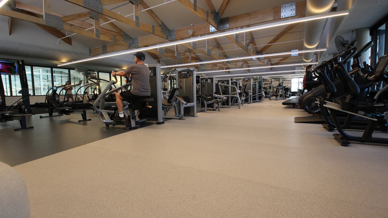 A closer look at the floor inside the gym at Yawa Aquatic Centre. There is a television mounted on the wall that keeps the gym members entertained while doing their exercises. There is enough space for people to walk and move all around the facility. Compared to the rubber mat floor in the previous image, the middle section is painted entirely black and looks smooth on the surface.